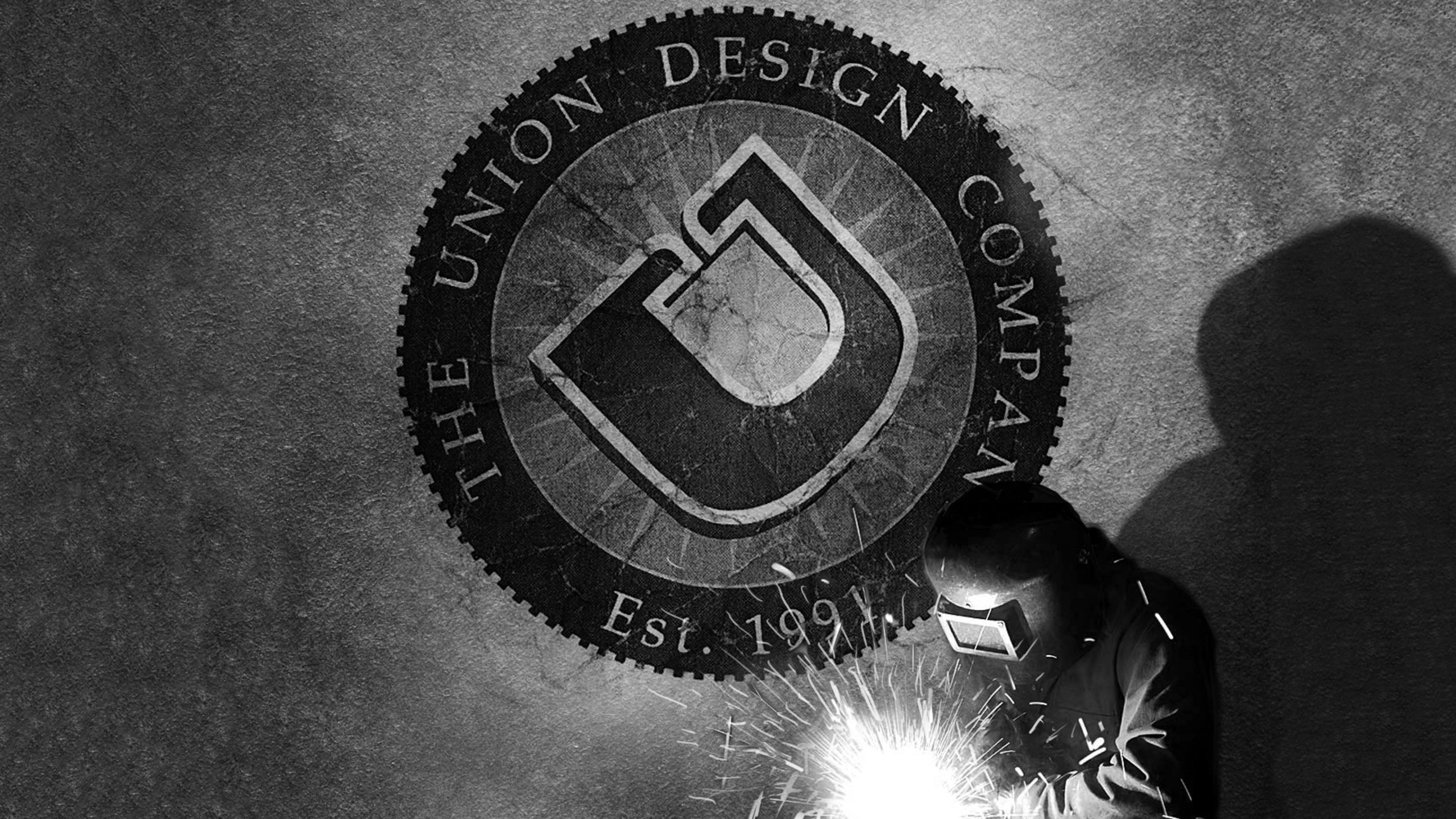 Dramatic black and white image of the union design company vintage logo on the wall with welder in the foreground.
